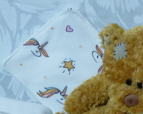 Un ours en peluche avec un mouchoir décoré de licornes et d’étoiles.