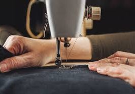 Main d'une personne utilisant une machine à coudre sur un tissu noir.